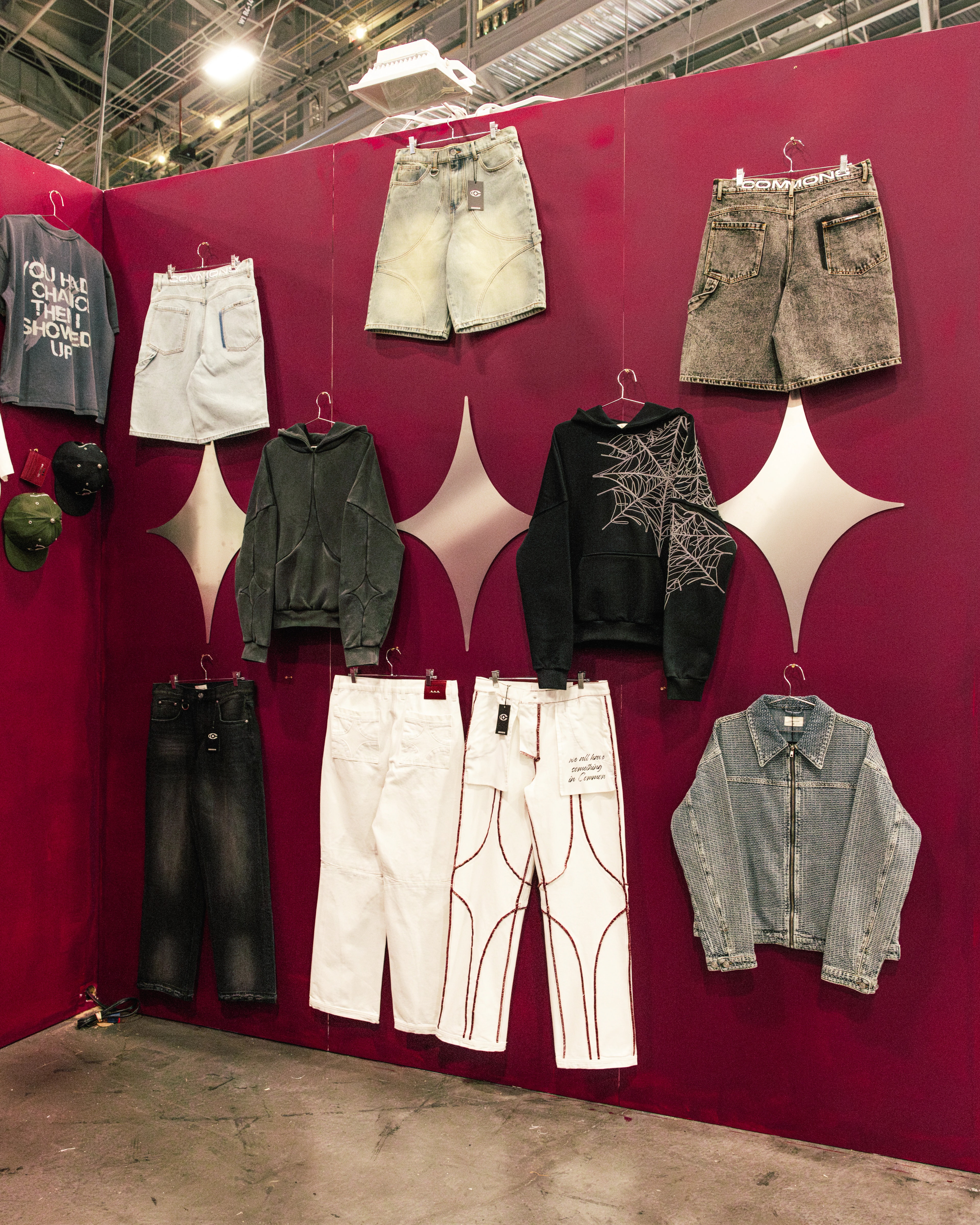 Commons Studios collection displayed on a trade show wall — denim, hoodies, and pants